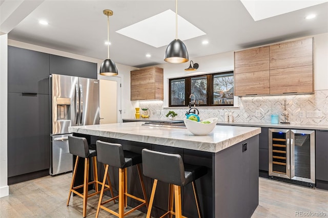 kitchen with beverage cooler, stainless steel fridge, backsplash, a kitchen island, and light stone counters