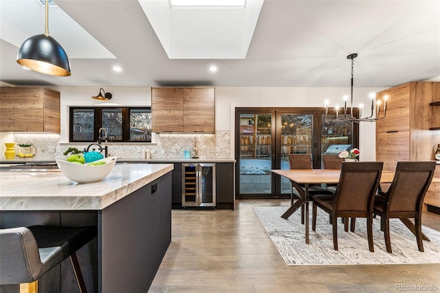 kitchen featuring brown cabinets, a notable chandelier, modern cabinets, backsplash, and wine cooler