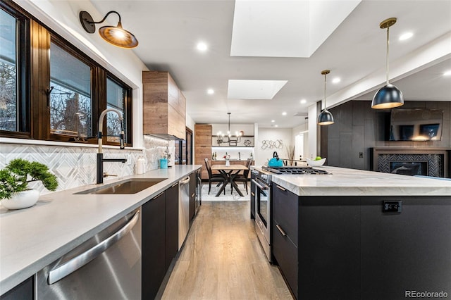 kitchen with modern cabinets, dark cabinets, a sink, appliances with stainless steel finishes, and a skylight