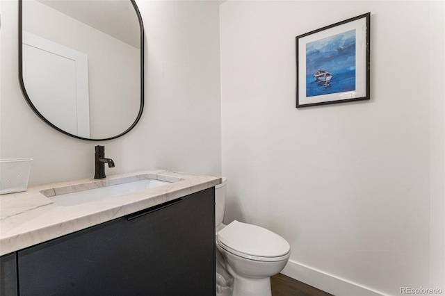 half bath featuring toilet, baseboards, wood finished floors, and vanity