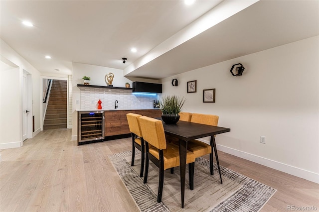 dining space with baseboards, wine cooler, wet bar, light wood-style floors, and recessed lighting