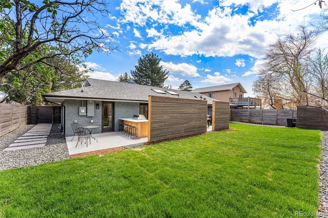 back of house with brick siding, a patio, a fenced backyard, a lawn, and a shingled roof