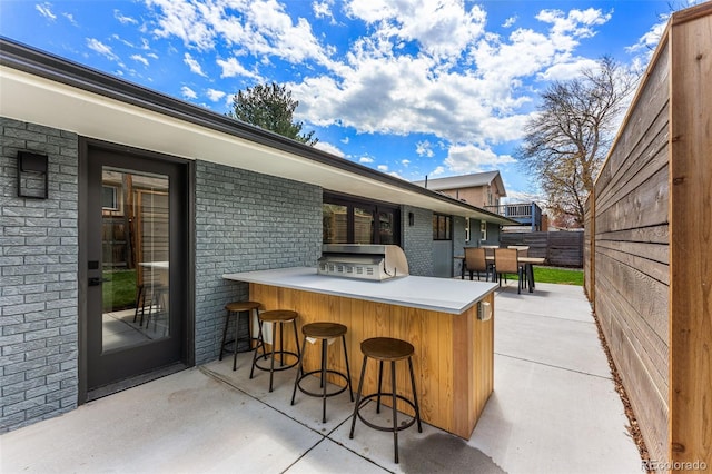 view of patio with outdoor dry bar, fence, and area for grilling