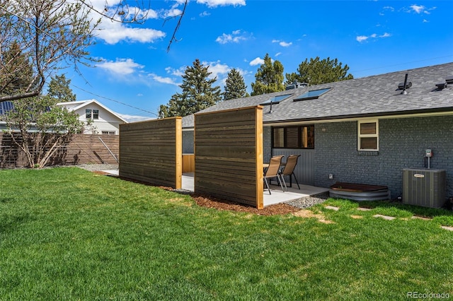 rear view of house with a yard, cooling unit, a patio, roof with shingles, and a fenced backyard