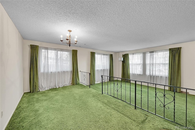 empty room with plenty of natural light, a textured ceiling, carpet, and a notable chandelier