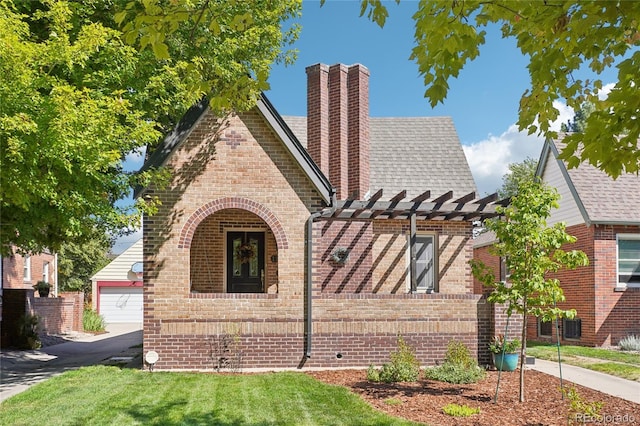 english style home featuring brick siding, a chimney, a shingled roof, and a pergola