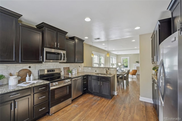 kitchen featuring visible vents, appliances with stainless steel finishes, a sink, light stone countertops, and a peninsula