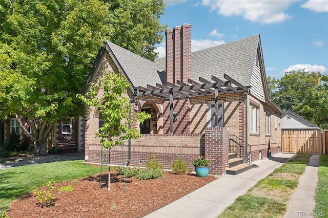 view of front facade featuring brick siding, a chimney, fence, a pergola, and a front yard