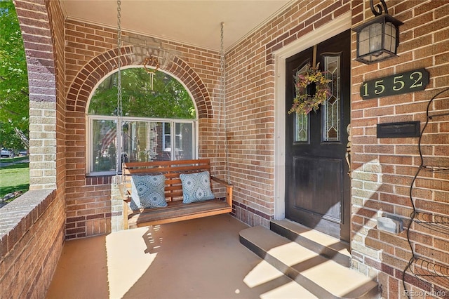 view of exterior entry with a porch and brick siding