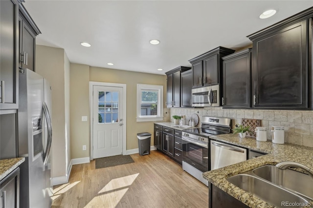 kitchen featuring decorative backsplash, light stone counters, stainless steel appliances, light wood-style floors, and a sink