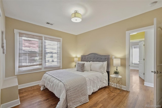 bedroom with wood finished floors, visible vents, and baseboards