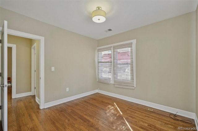 spare room featuring wood finished floors, visible vents, and baseboards