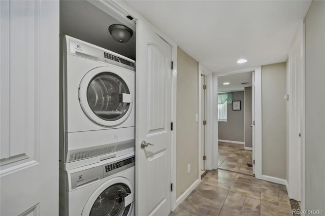 laundry area featuring light tile patterned floors, recessed lighting, stacked washing maching and dryer, laundry area, and baseboards