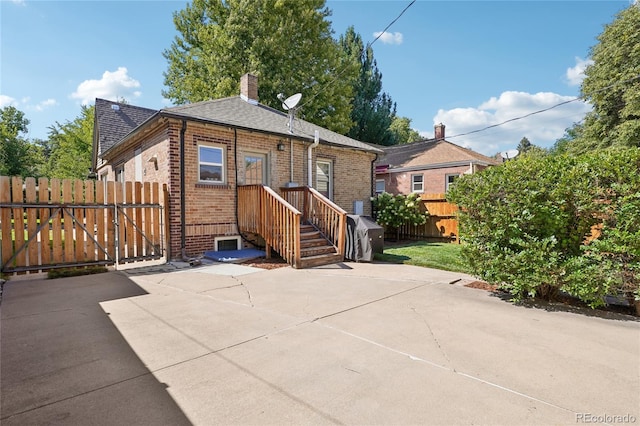 back of property featuring brick siding, roof with shingles, a chimney, a gate, and fence