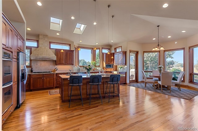 11541 Warrington Ct, Parker, CO 80138 - kitchen with a center island with sink, stainless steel appliances, wall chimney exhaust hood, light wood-type flooring, and recessed lighting