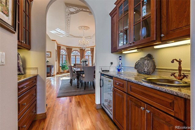 11541 Warrington Ct, Parker, CO 80138 - bar area featuring wine cooler, a sink, a chandelier, light wood-style flooring, and arched walkways