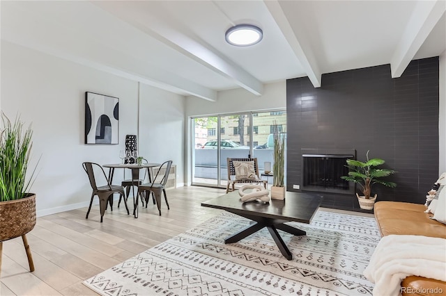 living room featuring tile walls, light hardwood / wood-style flooring, beamed ceiling, and a large fireplace