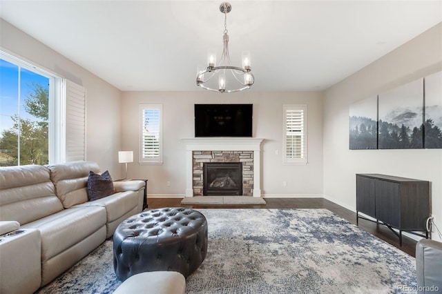 living room featuring dark wood-type flooring, a chandelier, and a stone fireplace