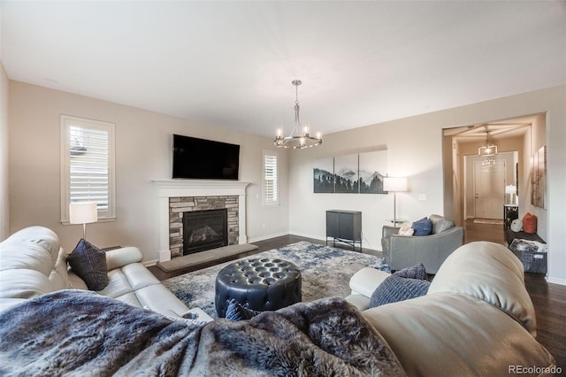 living room with dark wood-type flooring, a notable chandelier, and a stone fireplace