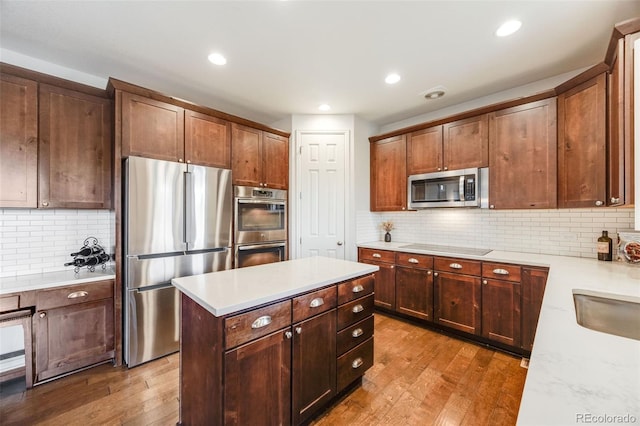 kitchen with light stone counters, stainless steel appliances, light hardwood / wood-style flooring, and backsplash