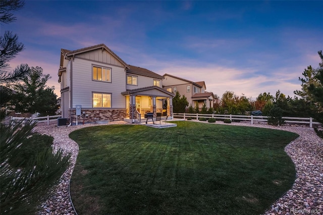 back house at dusk with a lawn, cooling unit, and a patio area