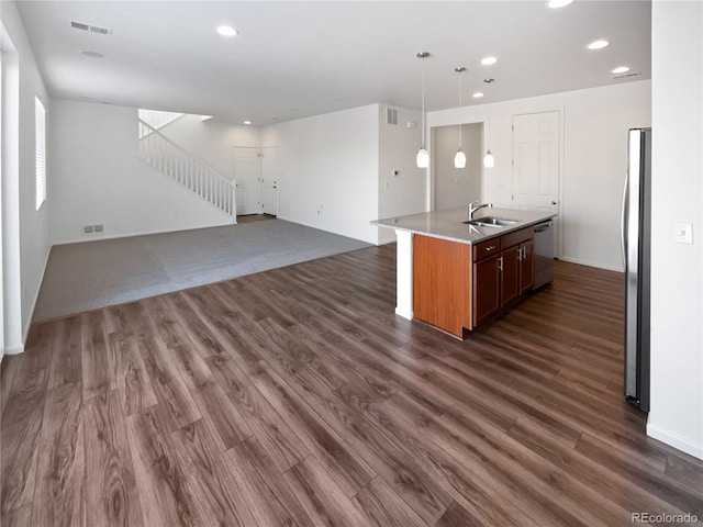 kitchen with appliances with stainless steel finishes, sink, hanging light fixtures, dark hardwood / wood-style floors, and a center island with sink