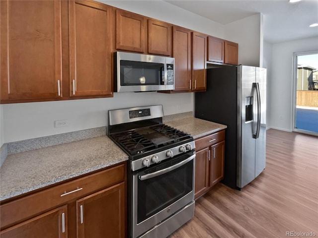 kitchen with light wood-type flooring, light stone countertops, and stainless steel appliances