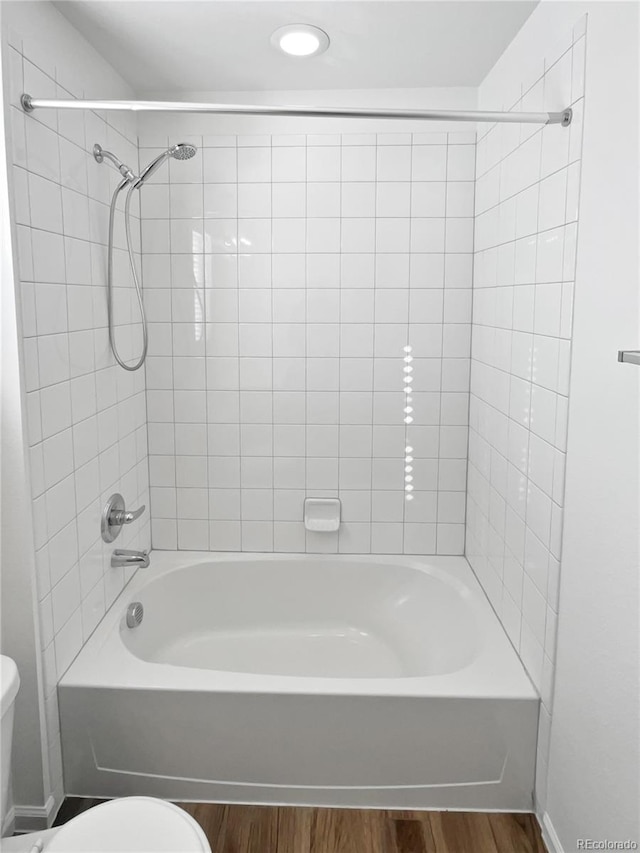 bathroom with hardwood / wood-style floors, toilet, and tiled shower / bath