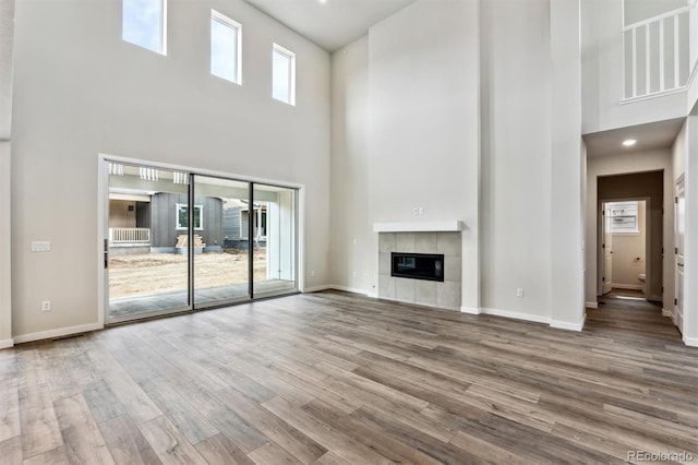 unfurnished living room with a tiled fireplace, a towering ceiling, baseboards, and wood finished floors