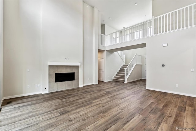 unfurnished living room featuring wood finished floors, a high ceiling, a fireplace, baseboards, and stairs