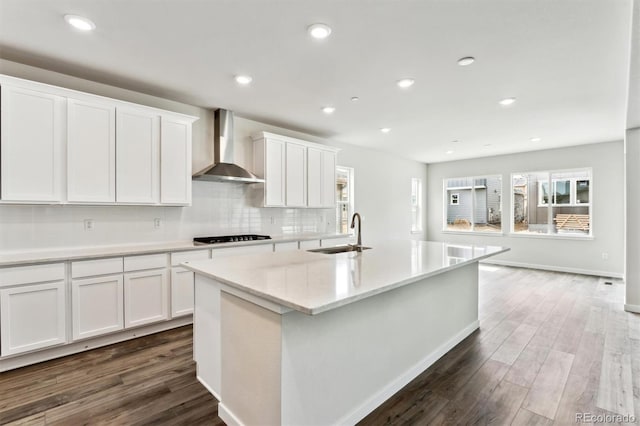 kitchen with a center island with sink, a sink, dark wood-style floors, white cabinetry, and wall chimney range hood