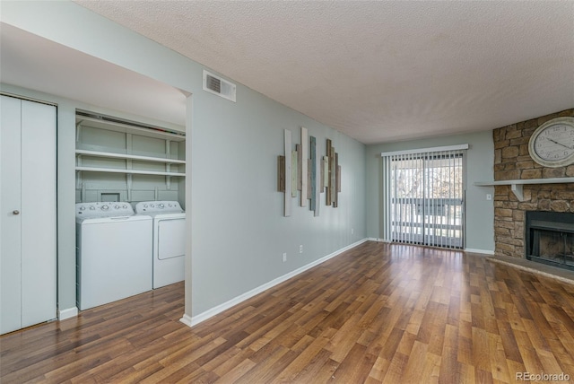 unfurnished living room with washing machine and clothes dryer, a stone fireplace, dark hardwood / wood-style flooring, and a textured ceiling