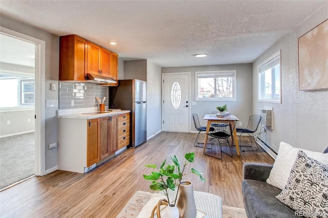 784 S 3rd Ave, Brighton, CO 80601 - kitchen featuring freestanding refrigerator, brown cabinets, light countertops, under cabinet range hood, and light wood-type flooring