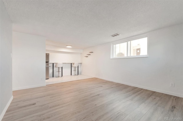 spare room featuring visible vents, a textured ceiling, baseboards, and wood finished floors