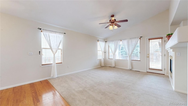 unfurnished living room with light carpet, baseboards, a glass covered fireplace, lofted ceiling, and ceiling fan