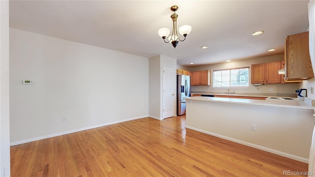 kitchen with stove, light countertops, light wood-type flooring, stainless steel refrigerator with ice dispenser, and a sink