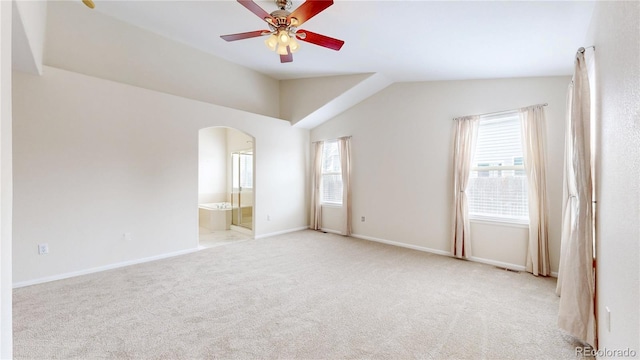 empty room featuring light carpet, arched walkways, baseboards, lofted ceiling, and ceiling fan