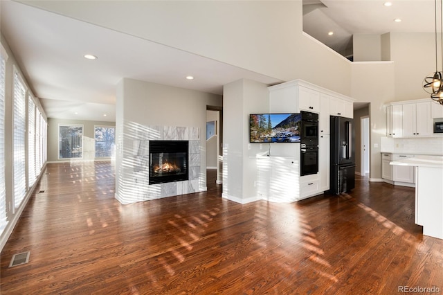 unfurnished living room with dark hardwood / wood-style flooring, a high ceiling, a high end fireplace, and a chandelier