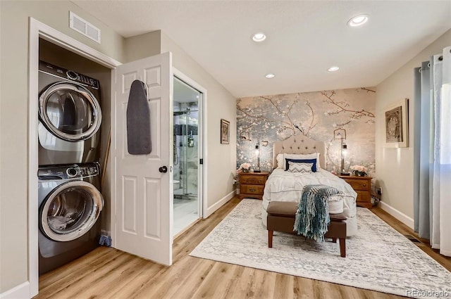 bedroom with hardwood / wood-style floors, stacked washing maching and dryer, and ensuite bath