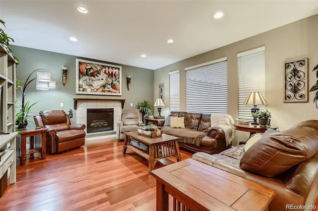 living room with a tiled fireplace and light wood-type flooring