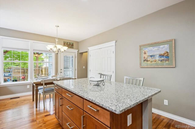 2723 Galena St, Denver, CO 80238 - kitchen with a chandelier, light wood finished floors, baseboards, light stone counters, and a kitchen island