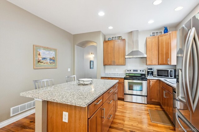2723 Galena St, Denver, CO 80238 - kitchen with stainless steel appliances, wall chimney exhaust hood, light wood-type flooring, arched walkways, and recessed lighting