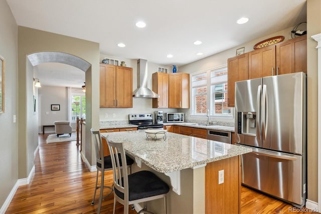 2723 Galena St, Denver, CO 80238 - kitchen with appliances with stainless steel finishes, wall chimney range hood, arched walkways, a kitchen island, and light wood-type flooring