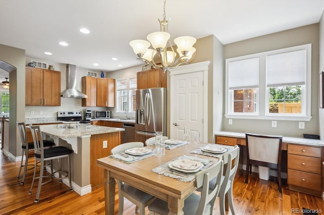 2723 Galena St, Denver, CO 80238 - kitchen with wall chimney exhaust hood, stainless steel appliances, a center island, brown cabinetry, and light wood-style flooring