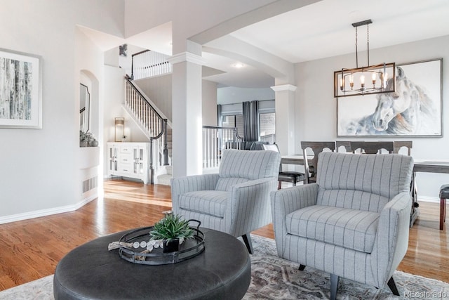 living room featuring light wood-type flooring, ornate columns, and a notable chandelier