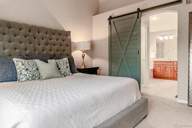 bedroom with ensuite bath, a barn door, and light colored carpet