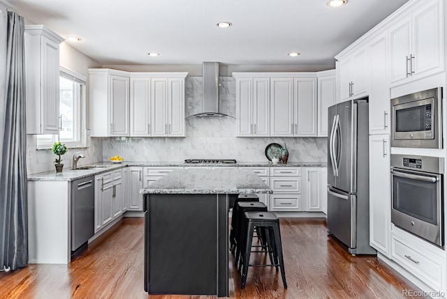 kitchen featuring appliances with stainless steel finishes, a kitchen breakfast bar, white cabinets, wall chimney range hood, and a kitchen island