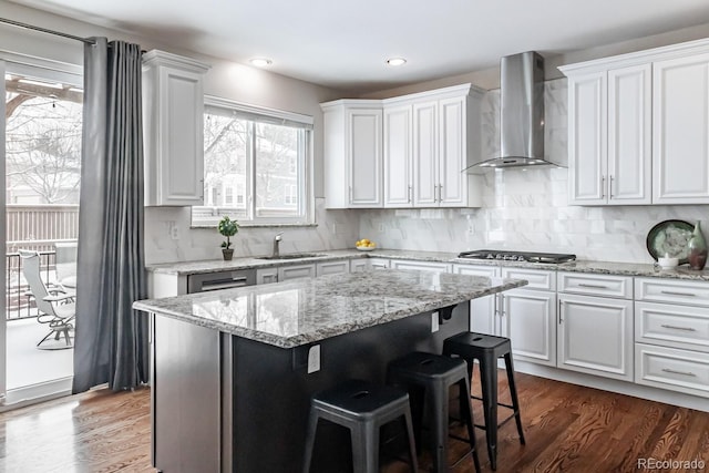 kitchen featuring white cabinets, wall chimney range hood, stainless steel gas stovetop, a center island, and sink