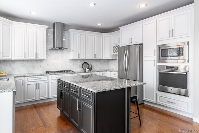 kitchen featuring white cabinetry, dark hardwood / wood-style flooring, a kitchen island, appliances with stainless steel finishes, and wall chimney exhaust hood