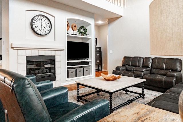 living room featuring a tiled fireplace, built in features, and hardwood / wood-style flooring